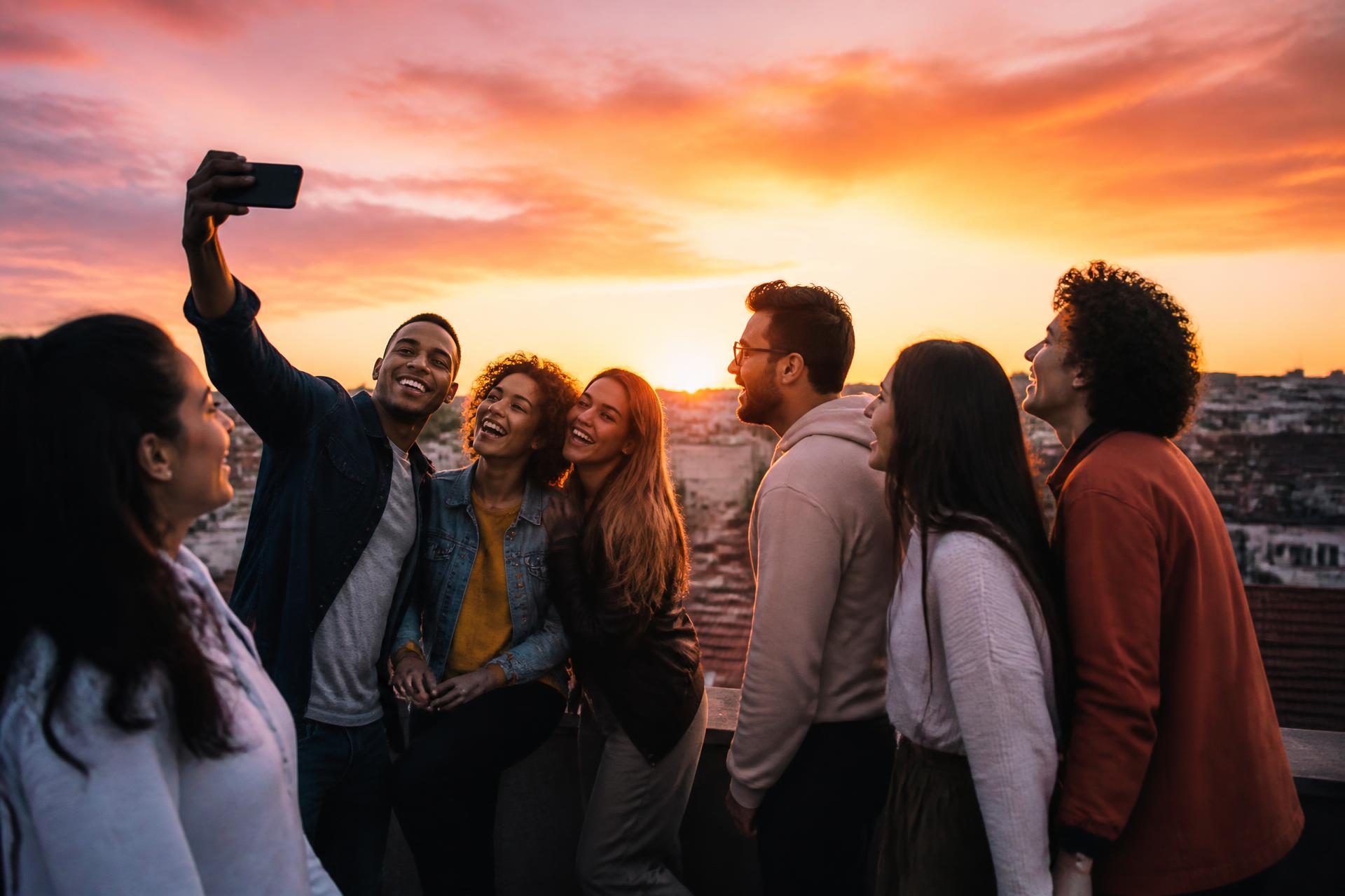Friends laughing together on a rooftop while sharing something on a phone